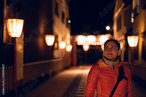 Kyoto, Japan narrow alley dark street in Gion district at night with young happy woman standing looking at illuminated row of red lanterns