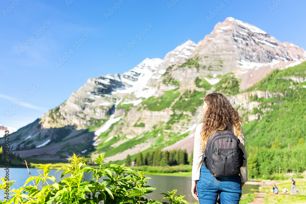 Aspen Maroon Bells rocky mountain peak with Creater Lake water in Colorado in summer and back of young woman hiker with backpack standing on trail