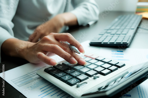 Fototapeta The hand of Asian woman is pressing calculator and prepare information for report to correct