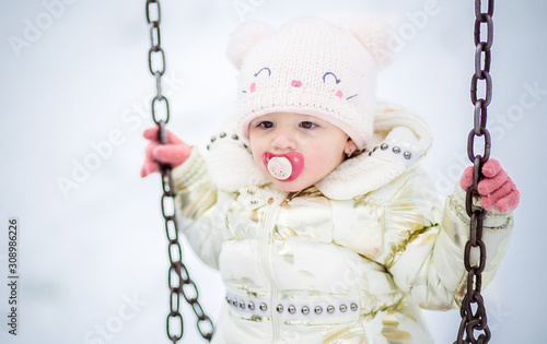 Cute litle girl on the swing, holding on to metal chains. Winetr clothing