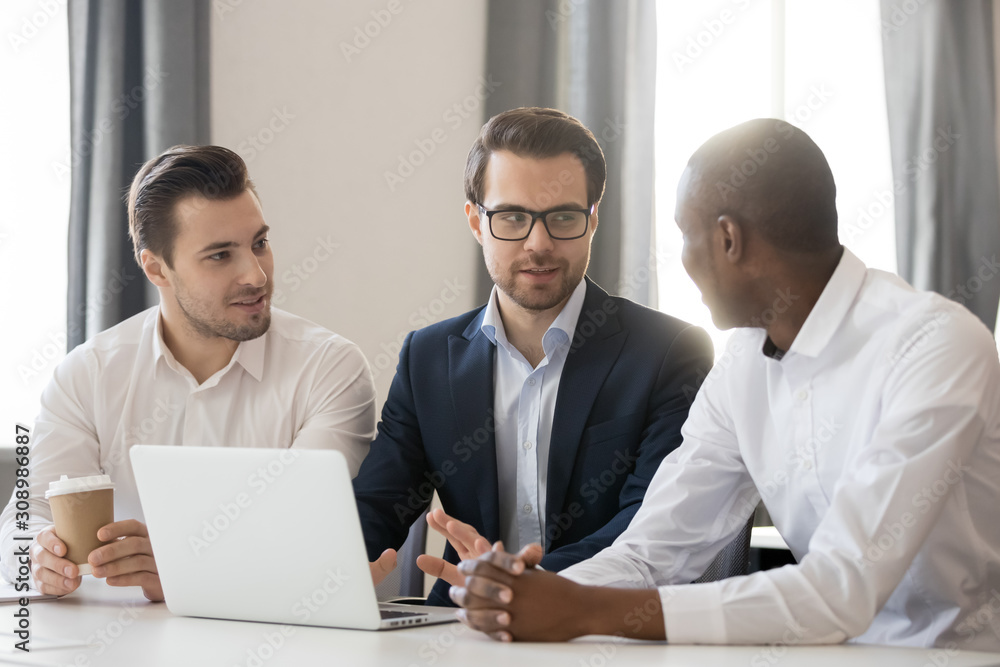 Obraz premium Diverse businessmen talk discussing ideas on laptop together