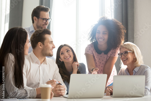 Smiling diverse employees laugh working together at laptop in office