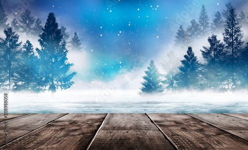 Winter background. Winter snow landscape with wooden table in front. Dark winter forest background at night. Snow, fog, moonlight. Dark neon night background in the forest with moonlight.  © MiaStendal