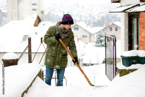 Man with shovel cleaning snow at day light in his backyard