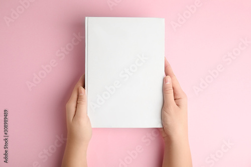 Woman holding book with blank cover on pink background, top view