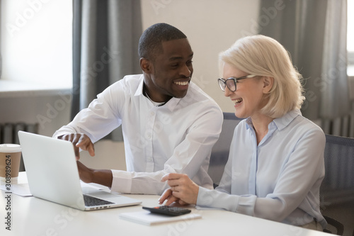 Smiling diverse workers laugh working on laptop together
