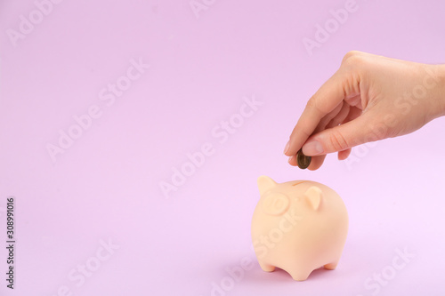 Woman putting coin into piggy bank on violet background, closeup. Space for text