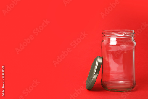 Open empty glass jar on red background, space for text