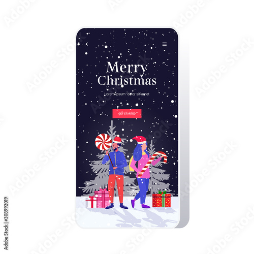 mix race couple in santa claus hats holding sweetmeats candy cane and lollipop merry christmas happy new year winter holidays celebration concept smartphone screen online mobile app full length vector