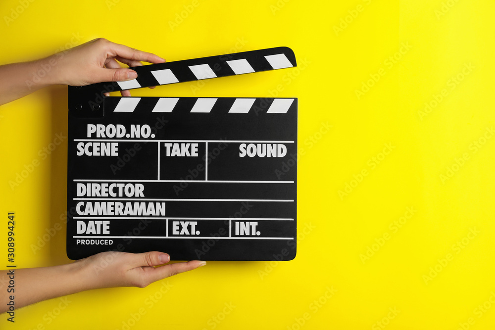 Woman holding clapperboard on yellow background, closeup with space for text. Cinema production
