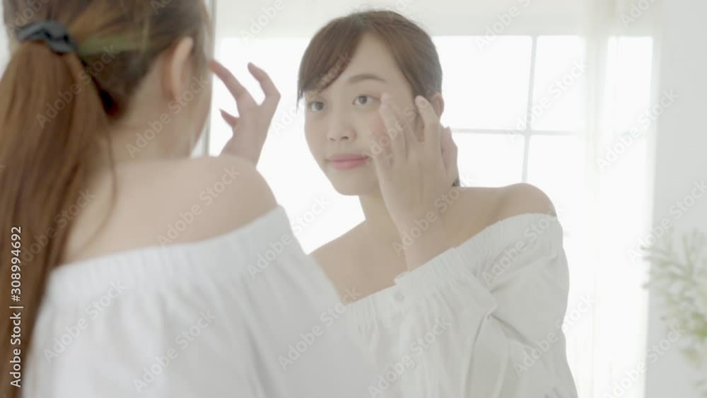 Beauty portrait young asian woman smiling look at mirror of checking skin care caucasian with wellness in the bedroom, beautiful girl happy face for health, lifestyle and wellbeing concept. Beauty portrait young asian woman smiling look at mirror of checking skin care caucasian with wellness in the bedroom, beautiful girl happy face for health, lifestyle and wellbeing concept.