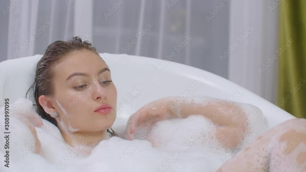 Beautiful Woman relaxing in bubble bath lying in bathtub. cheerful and relaxed lying in bathtub having foam bubbles bath at home or hotel bathroom smiling playful enjoying luxury lifestyle Beautiful Woman relaxing in bubble bath lying in bathtub. cheerful and relaxed lying in bathtub having foam bubbles bath at home or hotel bathroom smiling playful enjoying luxury lifestyle