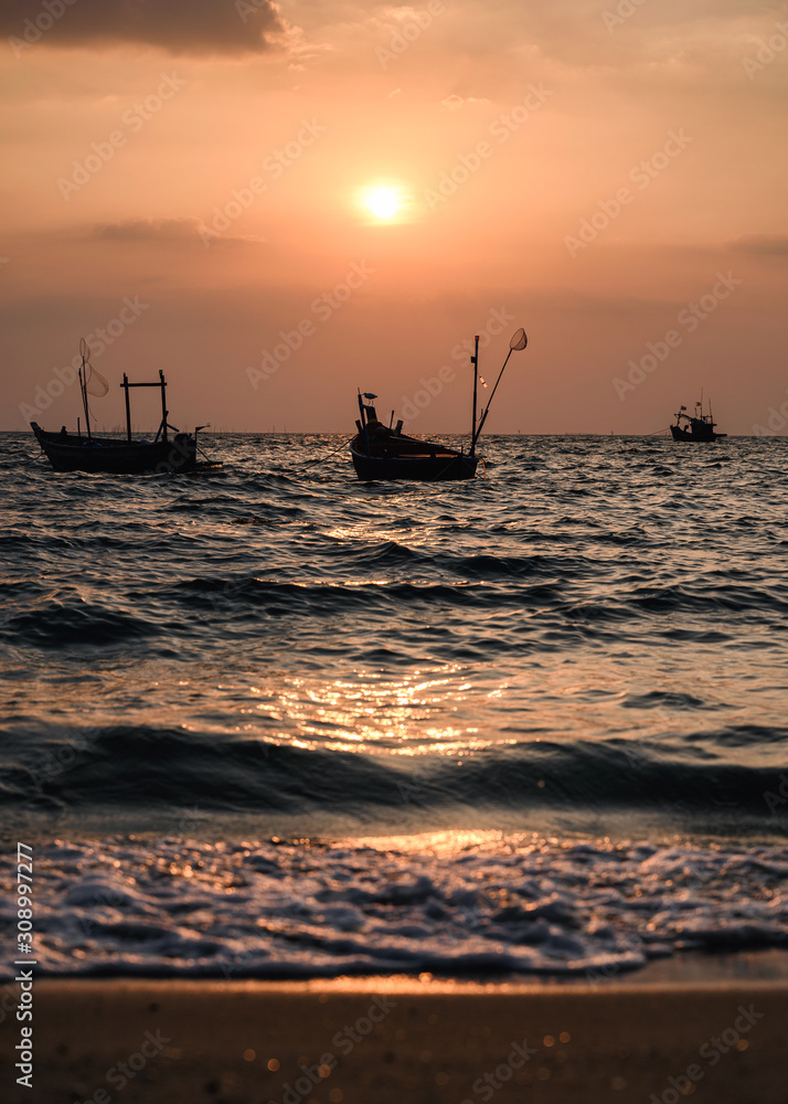 Fishing boat floating on tropical sea beach at sunset