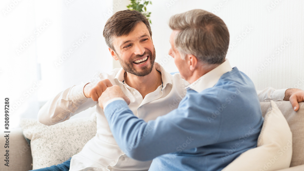 Man And Senior Father Bumping Fists Sitting On Sofa, Panorama Man And Senior Father Bumping Fists Sitting On Sofa, Panorama