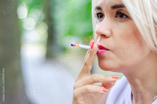 A woman smokes a cigarette. Holds in the mouth, red lips photo