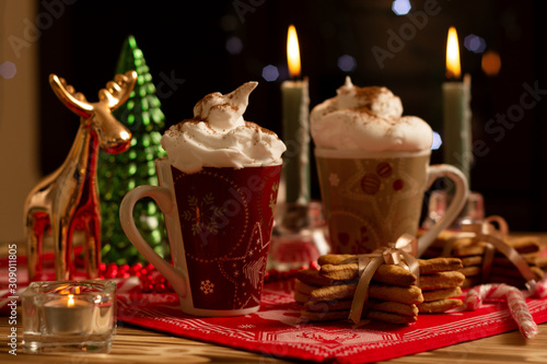 Horizontal view of hot spicy cinnamon creamy drinks in Christmas mug with burning candles and decorations