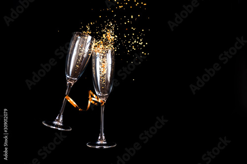 Two champagne glasses with golden sparkles over black background. Happy new year. photo