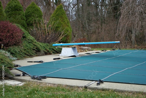 backyard swimming pool with diving board and pool slide tarped up and closed down for winter