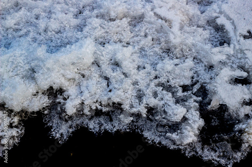 Picturesque hoarfrost, crystals on river ice over dark water. Dark and light beautiful. The structure of snow and ice. Close-up. Selective, soft focus.