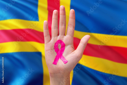 Aland Islands awareness concept. Close-up awareness ribbon painted on palm on national flag background. October Pink day and world cancer day.