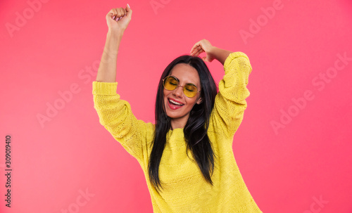 Dancing exciting. Close-up photo with a merry young girl in a yellow knitted sweatshirt and yellow glasses, who is dancing with her hands in the air.