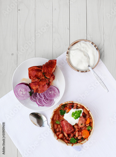 Canvas Print Pinto bean soup with smoked ham hock in bowl with sour cream and red onions on t