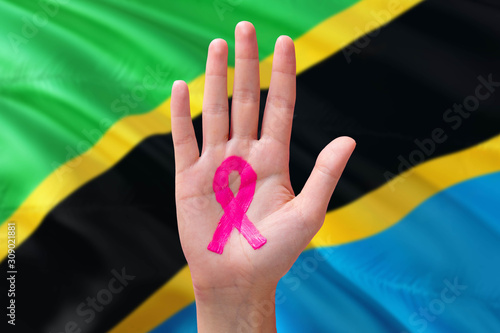 Tanzania awareness concept. Close-up awareness ribbon painted on palm on national flag background. October Pink day and world cancer day.
