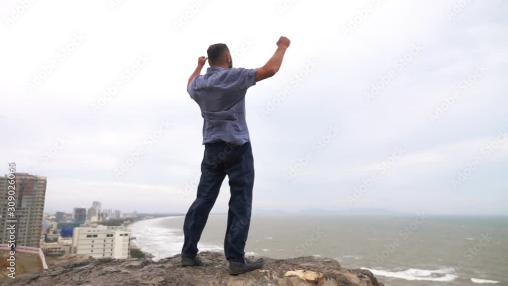 Excited, successful man rising arms on cliff above city, super slow motion Excited, successful man rising arms on cliff above city, super slow motion