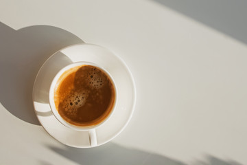 Cup of coffee atanding on the white table in sunlight