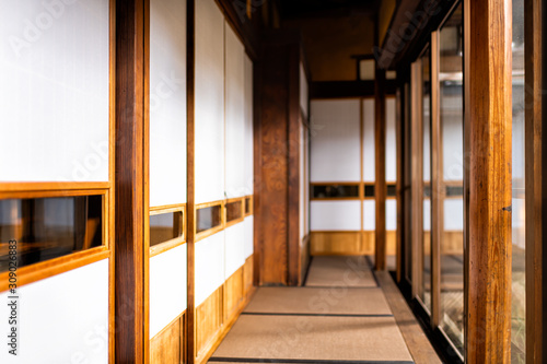 Traditional japanese home or ryokan with shoji sliding paper doors tatami mat floor in corridor hallway leading to room by glass windows