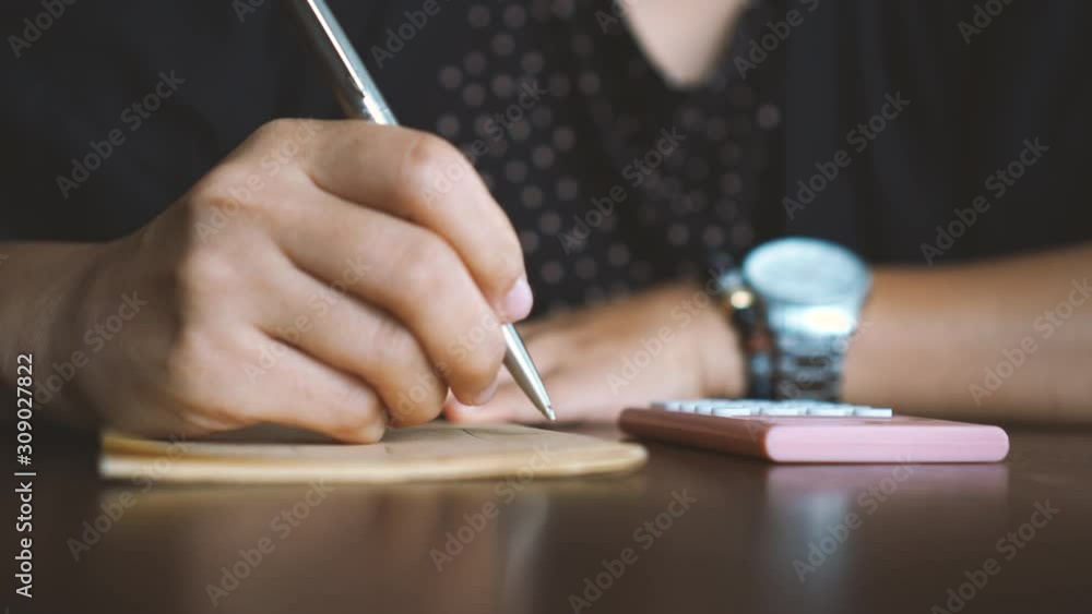4k video woman hand writing down in white notebook while using calculator to plan work on table with bokeh light in cafe background. 4k video woman hand writing down in white notebook while using calculator to plan work on table with bokeh light in cafe background.