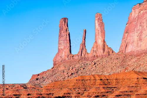 Closeup view of famous mesa butte three sisters formations with red orange rock color in Monument Valley canyons during sunrise in Arizona