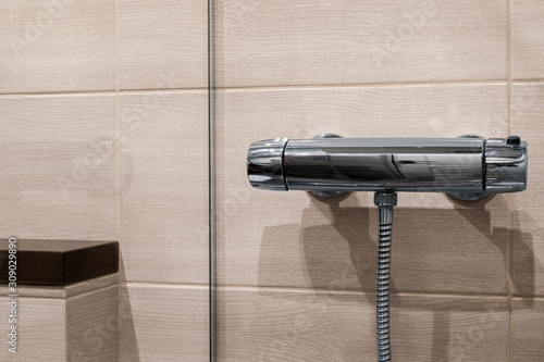 Thermostatic shower faucet on beige  the wall in bathroom. Shelf behind glass wall. photo