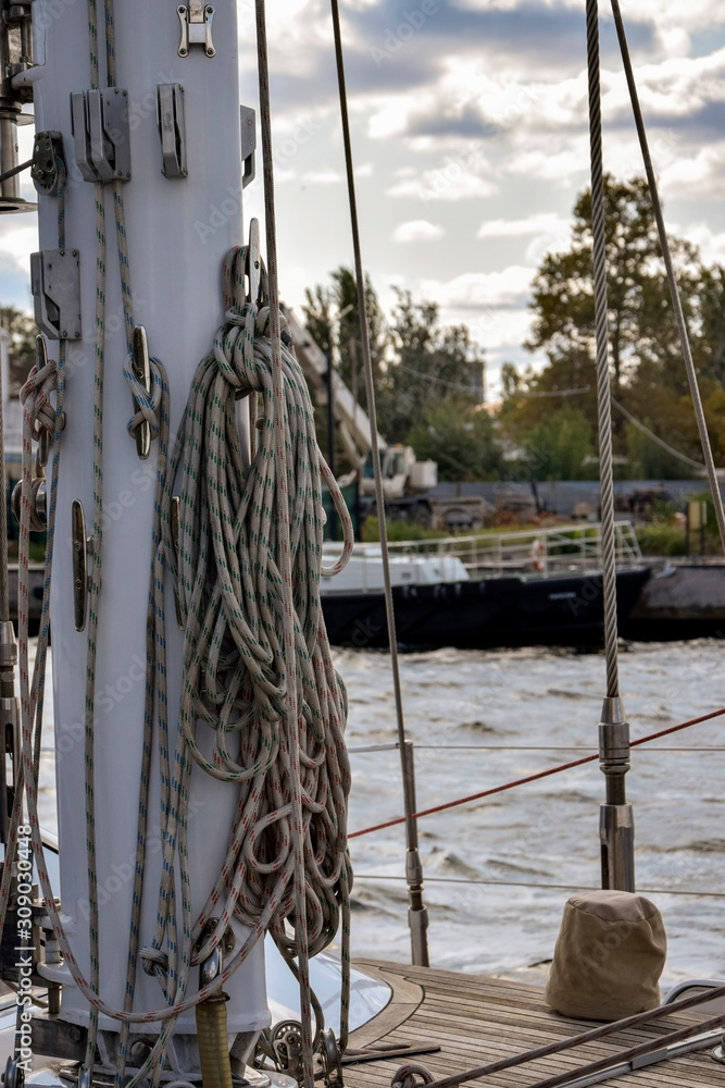 Obraz premium Fragment of a mast rigging a sailing yacht against the background of a river and cloudy sky. Close-up.