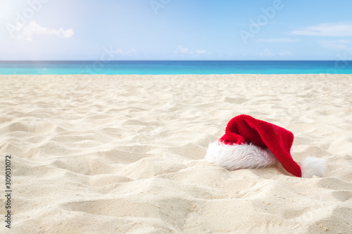 Close up Santa hat on a white sandy infinity caribbean beach . Christmas Holiday Travel Concept