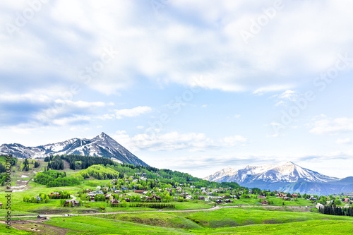 Mt Crested Butte panoramic snow mountain view with cloudy sky in lush green grass summer with houses buildings in small town village