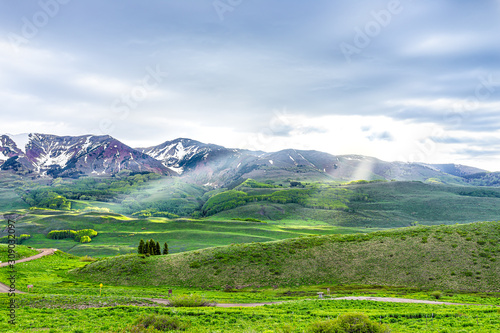Mount Crested Butte, Colorado alpine meadows view from Snodgrass hiking trail in summer with green grass and sun rays through clouds with gothic road