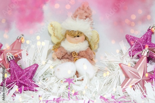 Plush fabric Christmas ornament little girl angel and star-shaped ornaments. Christmas still life.Stars baubles in purple tones and pink-white baby girl angel under the lights.