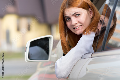 Young woman driving a car backwards. Girl with funny expression on her face while she made a fender bender damage to a rear vehicle.