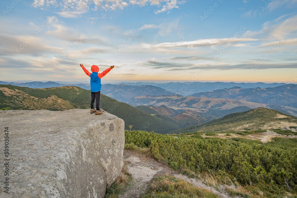 Obraz premium Young child boy hiker standing with raised hands in mountains enjoying view of amazing mountain landscape at sunset.
