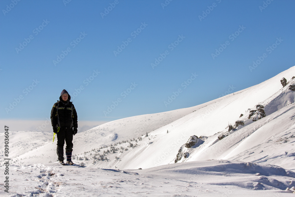 Silhouette of alone tourist standing on snowy mountain top enjoying view and achievement on bright sunny winter day. Adventure, outdoors activities and healthy lifestyle concept.