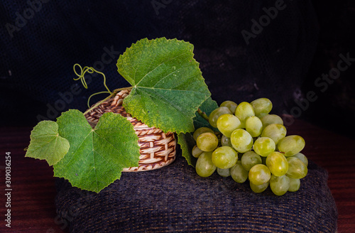 white clusters of grapes with green leaves lie next to a wicker small basket