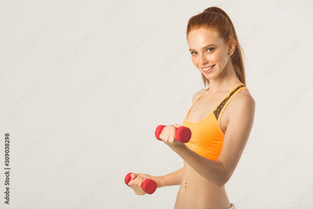 beautiful young woman with red hair with dumbbells in hands on a white background beautiful young woman with red hair with dumbbells in hands on a white background
