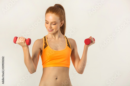 beautiful young woman with red hair with dumbbells in hands on a white background