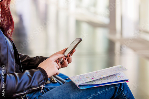 Passenger traveler woman using smart phone in airport holding a map. Clouse up of a young woman holding a map and using cell phone serching for answer on internet.