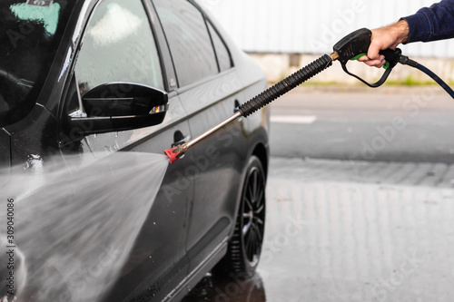 A man is washing a car at self service car wash. High pressure vehicle washer machine clean with water. Car wash equipment