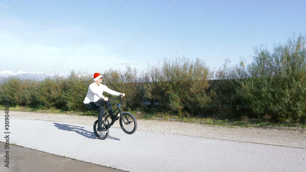 Obraz premium Extreme bmx biker riding manual trick in sunny park with santa claus hat