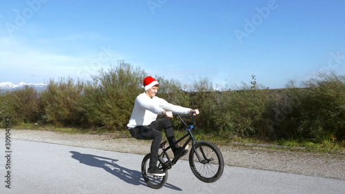 Young extreme bmx biker riding manual trick with santa claus hat