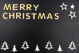 The Inscription Merry Christmas made of wooden letters, lying flat from above, isolated on a black, rough background. White wooden Christmas trees arranged in a row at the bottom.