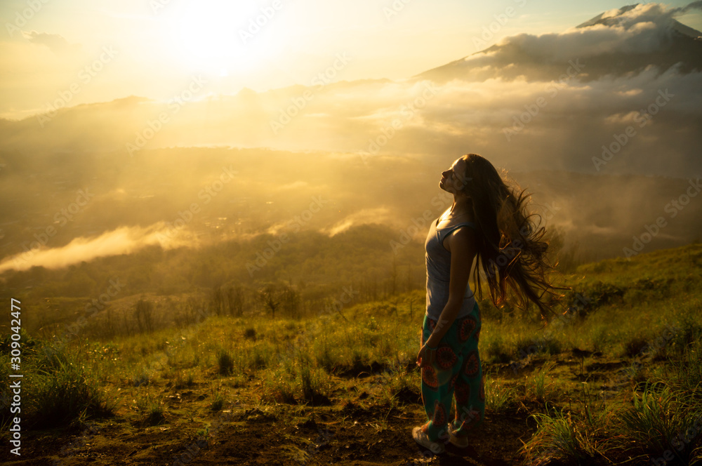 Fototapeta premium Beautiful girl with long hair on the volcano Batur on the island of Bali. Indonesia at sunrise. A lot of sun